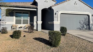 A residential house with a garage, a covered patio with chairs, and a gravel driveway. - Spacious, Family-Friendly Home in Maricopa (Maricopa)