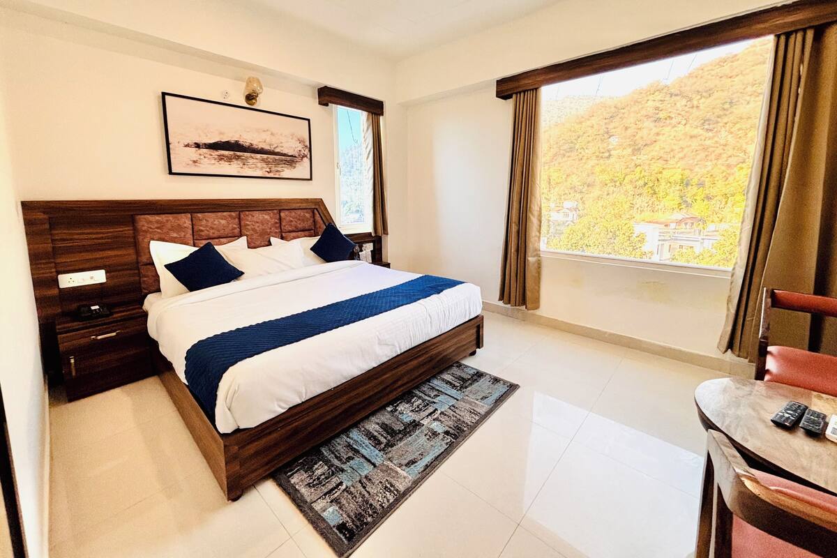 A hotel room with a large bed, a desk, and a window with a view of a hillside.