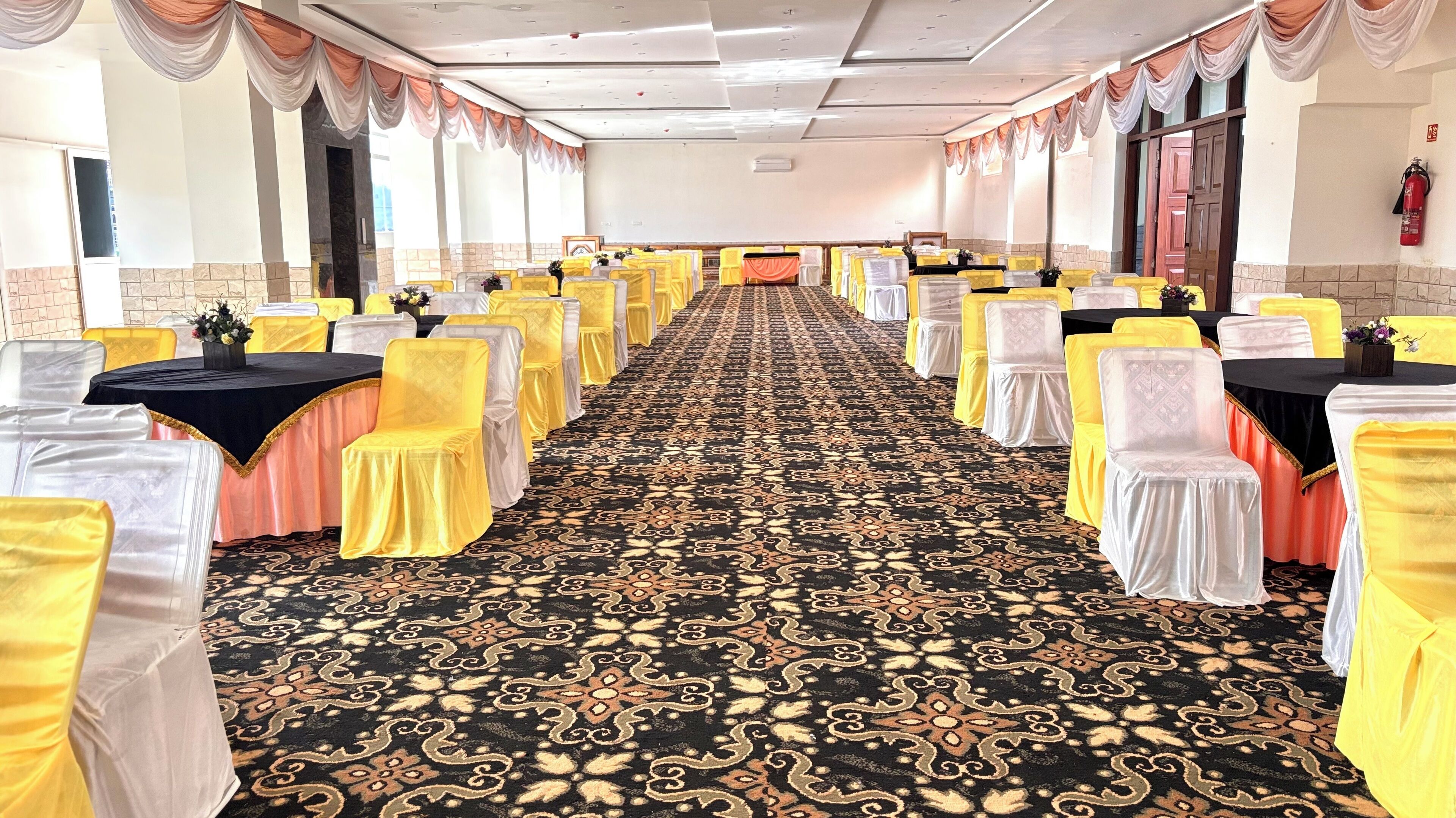 A banquet hall with rows of tables and chairs, a patterned carpet, and draped curtains.