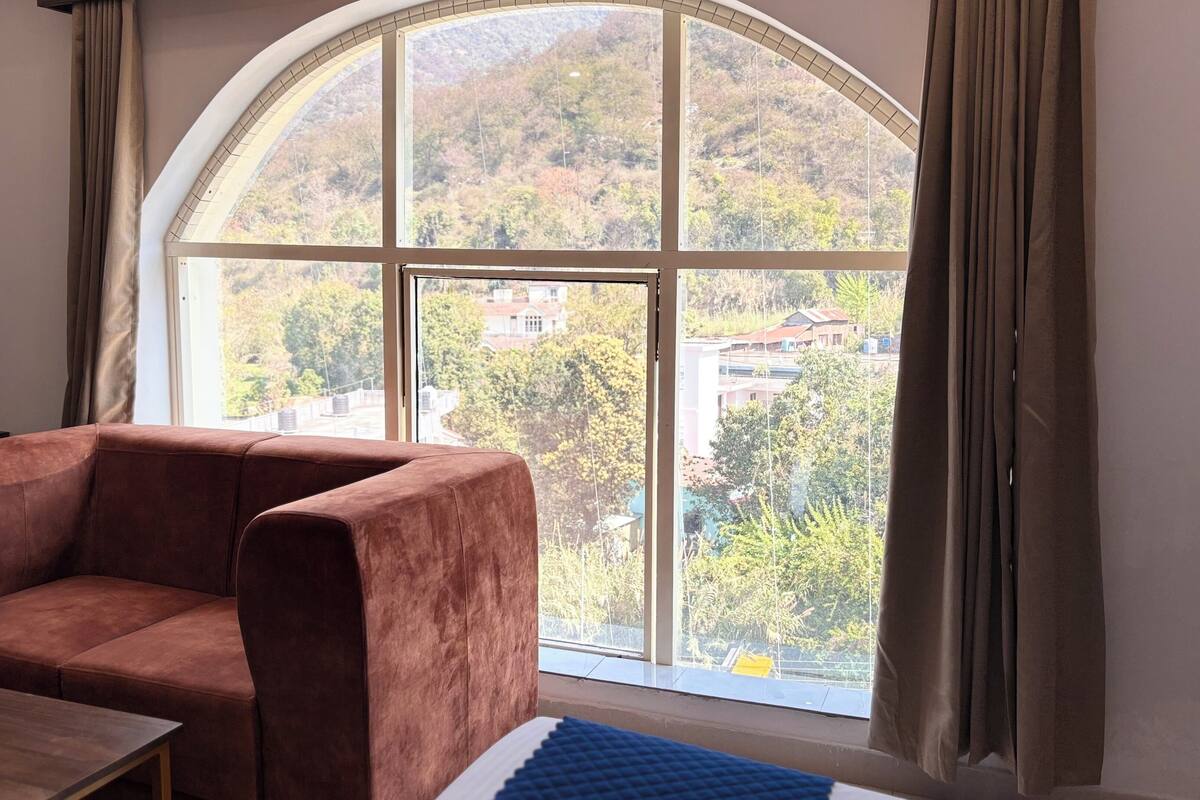 A room with a large arched window, a brown sofa, a small table, and a blue rug.