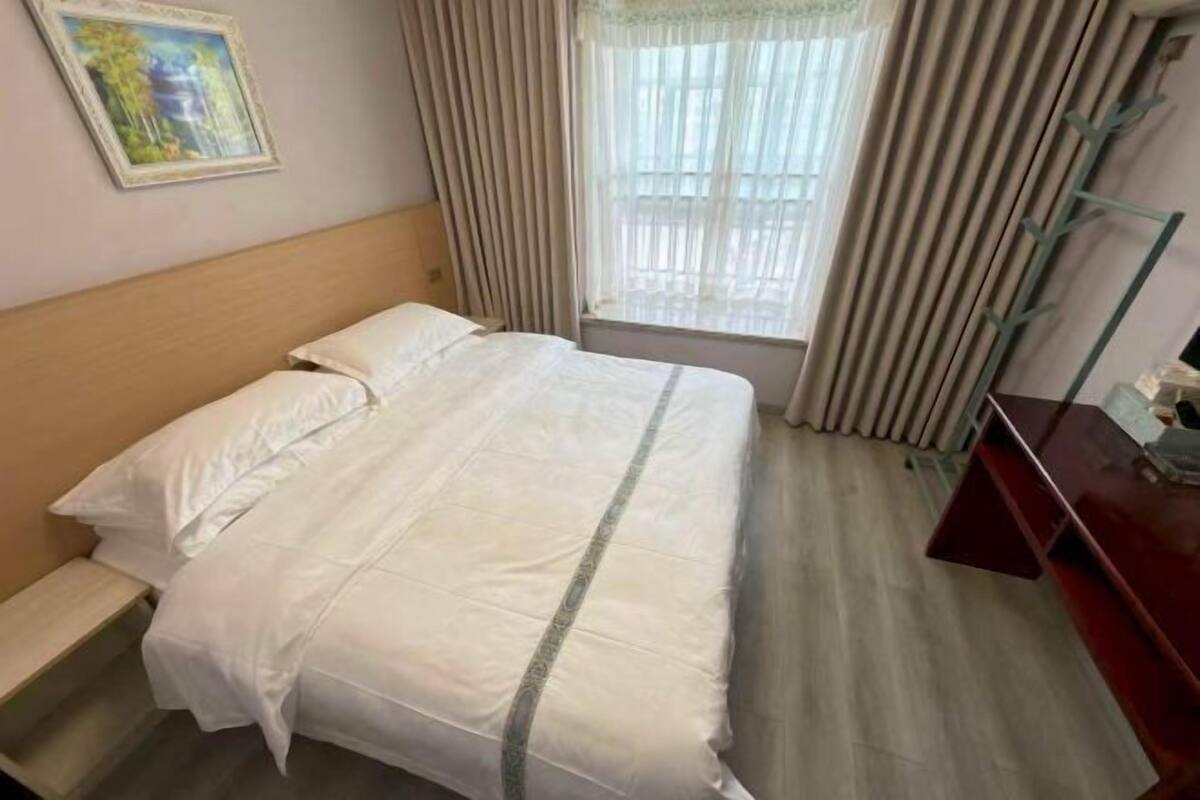 Een hotelkamer met een bed, een raam met gordijnen, een bureau en een schilderij aan de muur.