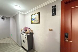 Un couloir avec une porte sur la droite, un panneau fixé au mur et un meuble orné de fleurs.