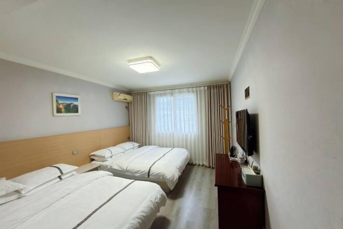 Een hotelkamer met twee bedden, een flatscreen televisie, een schilderij aan de muur en een raam met gordijnen.