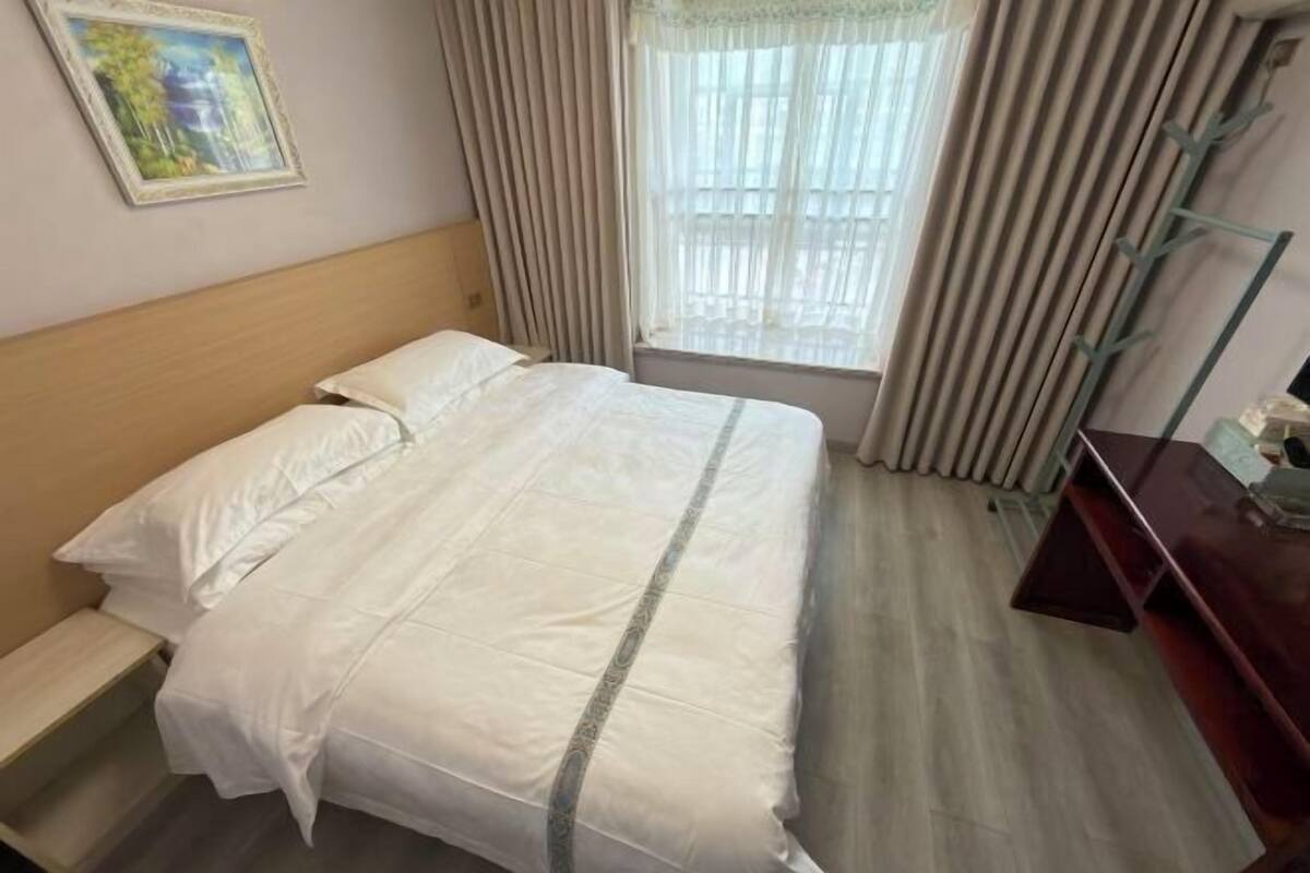 Een hotelkamer met een bed, een raam met gordijnen, een nachtkastje en een aan de muur hangend schilderij.