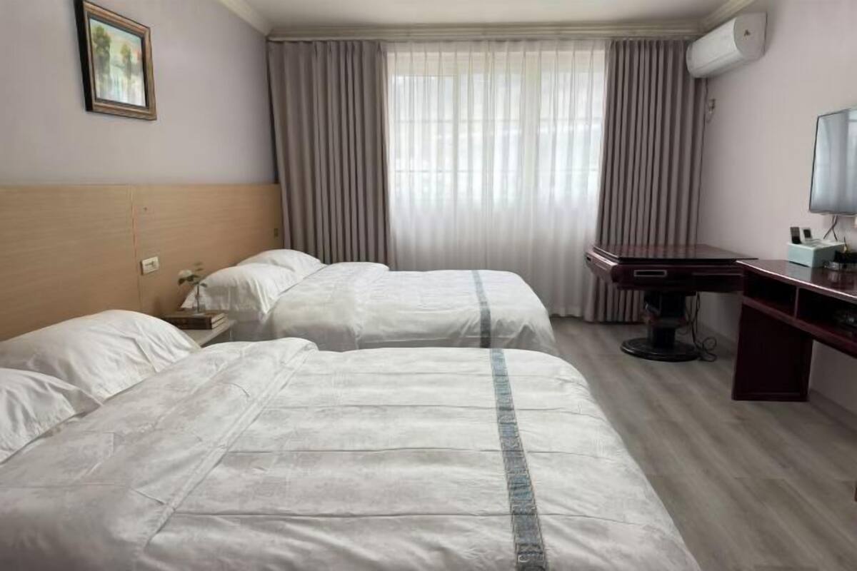 Hotelkamer met twee bedden, een bureau, een stoel, een televisie en een raam met gordijnen.