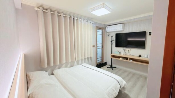 A hotel room with a bed, a flat-screen TV mounted on the wall, a desk with a chair, and a window with curtains.