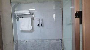 A glass-enclosed shower area with a white towel, soap dispensers, and a tiled wall.