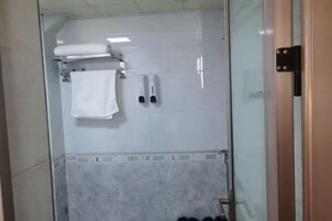 Área de chuveiro com paredes de vidro, uma toalha branca, dosadores de sabonete e parede revestida de azulejos.