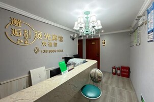 Uma área de recepção com balcão de mármore, uma placa verde, um candelabro e extintores.