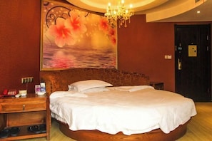 A bedroom with a round bed, a nightstand, a wooden dresser, and a large floral artwork on the wall. - Caizi Jiaren Hotel (Leping)
