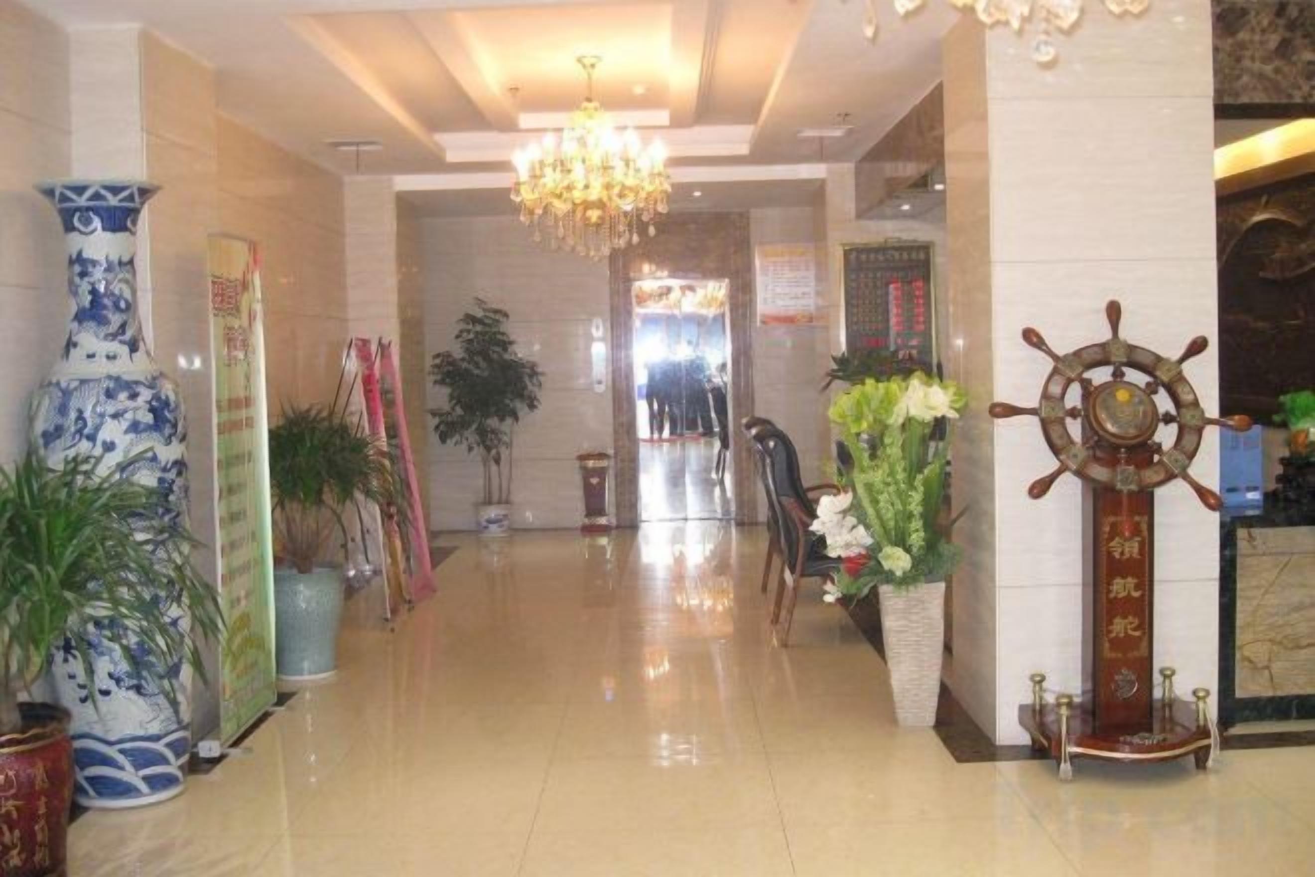 A hotel lobby with a chandelier, potted plants, and a ship's wheel decoration.