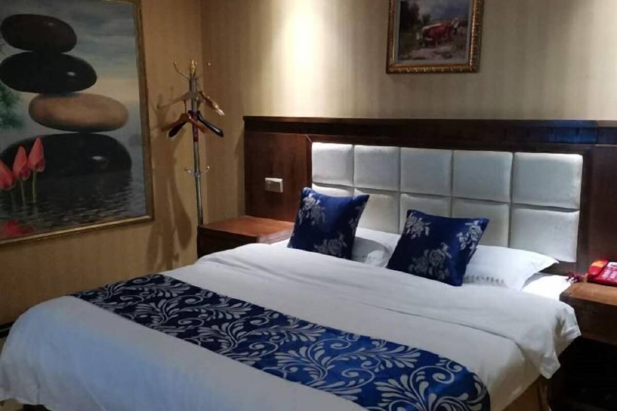 Habitación de hotel con una cama, una mesita de noche, un perchero en la pared y un cuadro.