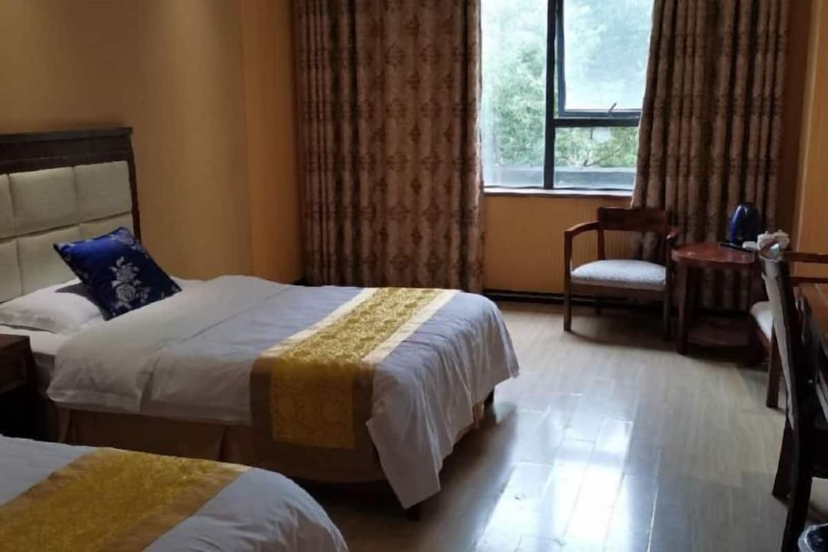 Habitación de hotel con dos camas, un escritorio, una silla y un ventanal con cortinas.
