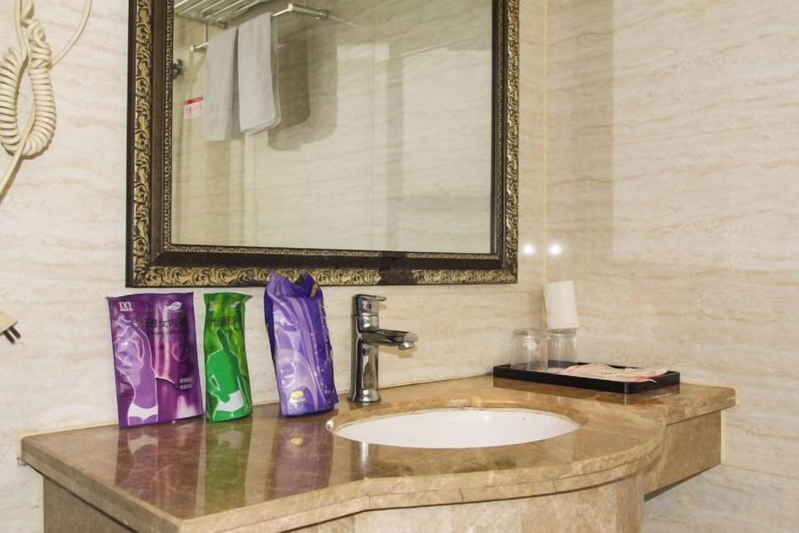 Un baño con lavamanos de mármol, un espejo con marco decorativo y tres neceseres sobre la encimera.