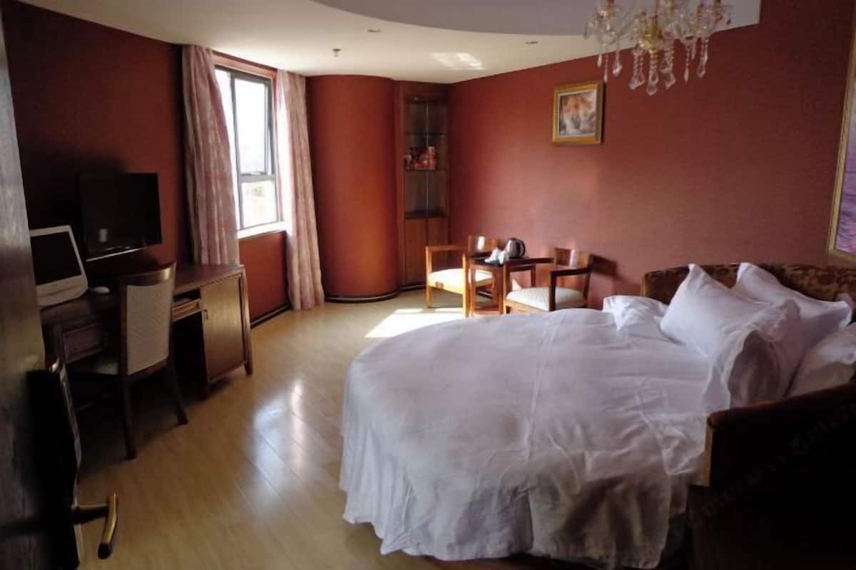 Una habitación de hotel con una cama, un escritorio con televisor, una silla, una mesita y una estantería.