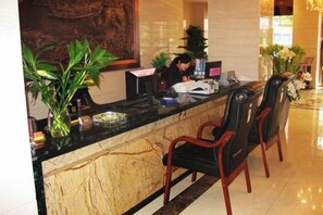 A hotel reception area with a marble counter, two black chairs, a receptionist, and a large painting on the wall. - Caizi Jiaren Hotel (Leping)