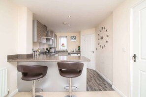 A modern kitchen with a central island, two bar stools, and a clock on the wall.