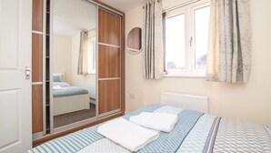 Un dormitorio con cama, armario, espejo y ventana con cortinas.