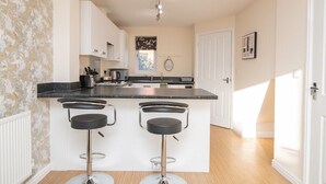 Una cocina moderna con una isla central, dos taburetes de bar, muebles blancos y una ventana con vistas.