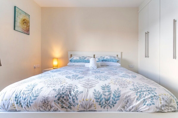 A bedroom with a bed, nightstand, wall art, and a wardrobe.