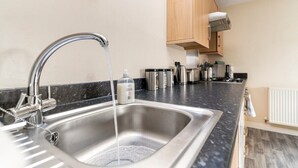 A kitchen with a stainless steel sink, a faucet, and a countertop with various kitchen items. - Lovely Two Bed detached house with Parking (Tipton)