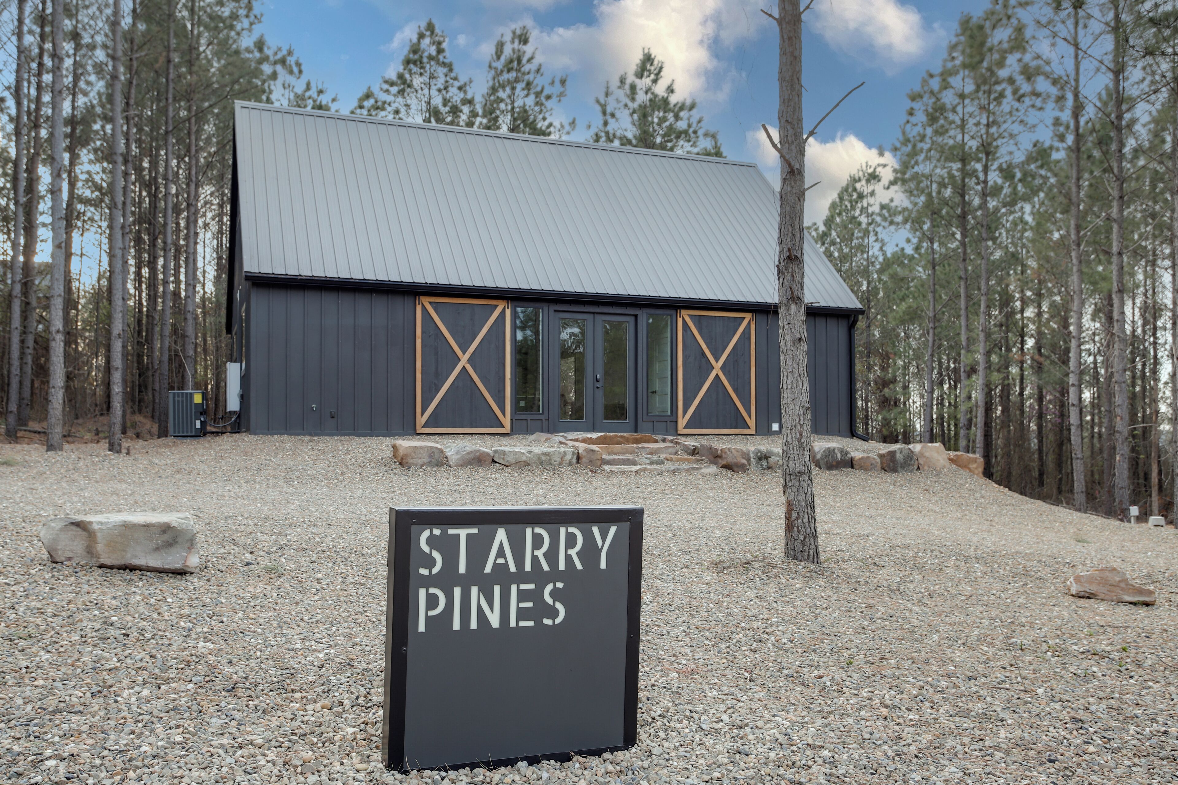 A building with a metal roof and large windows, surrounded by trees, with a sign reading "STARRY PINES".