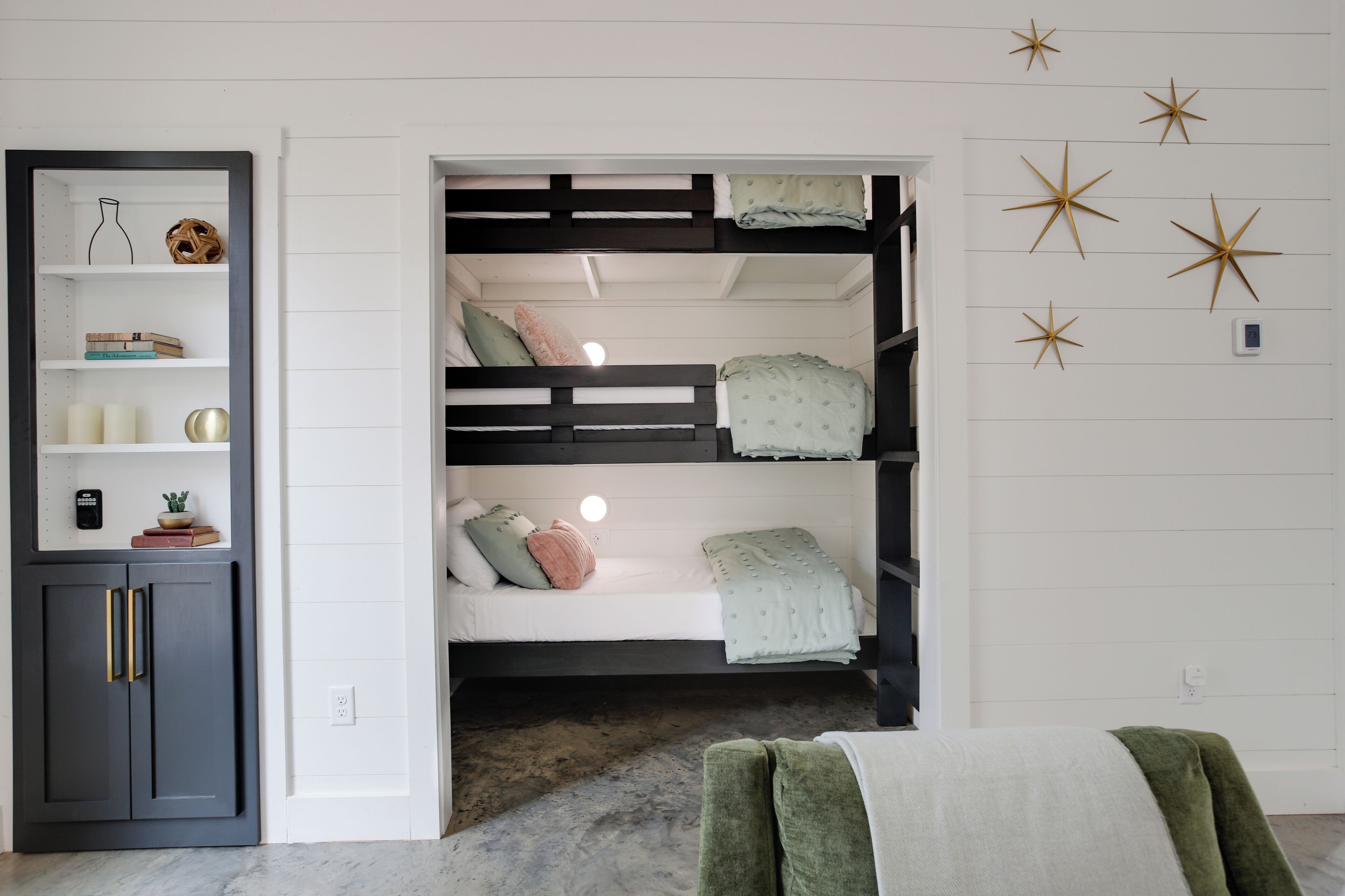 Ein Schlafraum mit Etagenbett und fest eingebautem Regalsystem, Wanddekoration mit Sternenmotiven und einem grünen Stuhl.