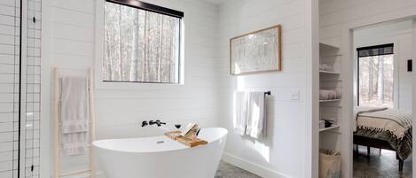 Un baño moderno con una bañera independiente, una escalera de madera y un amplio ventanal que proporciona luz natural.