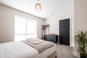 Ein Schlafzimmer mit einem Bett, einem Schminktisch, einem Spiegel, einer Tür und einer Zimmerpflanze.