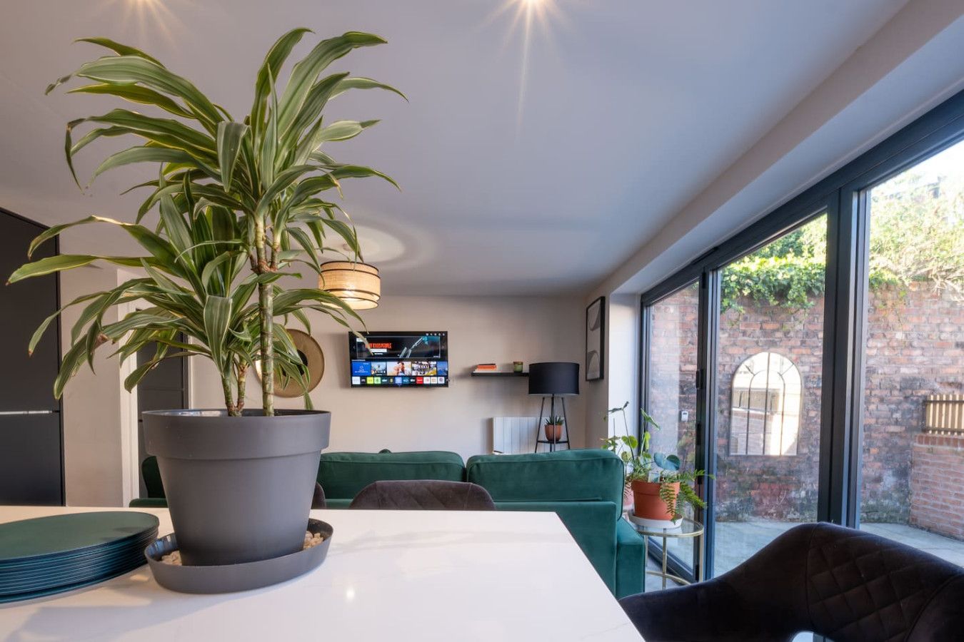 Un saló modern amb una gran planta en test, un televisor de pantalla plana i un sofà verd.