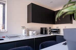 A modern kitchen with black cabinets, a white countertop, a kettle, a toaster, a coffee maker, and a microwave. - Luxury City Centre 4BR House | Sleeps 10 | Free Parking By Torr Property Group (Merseyside)