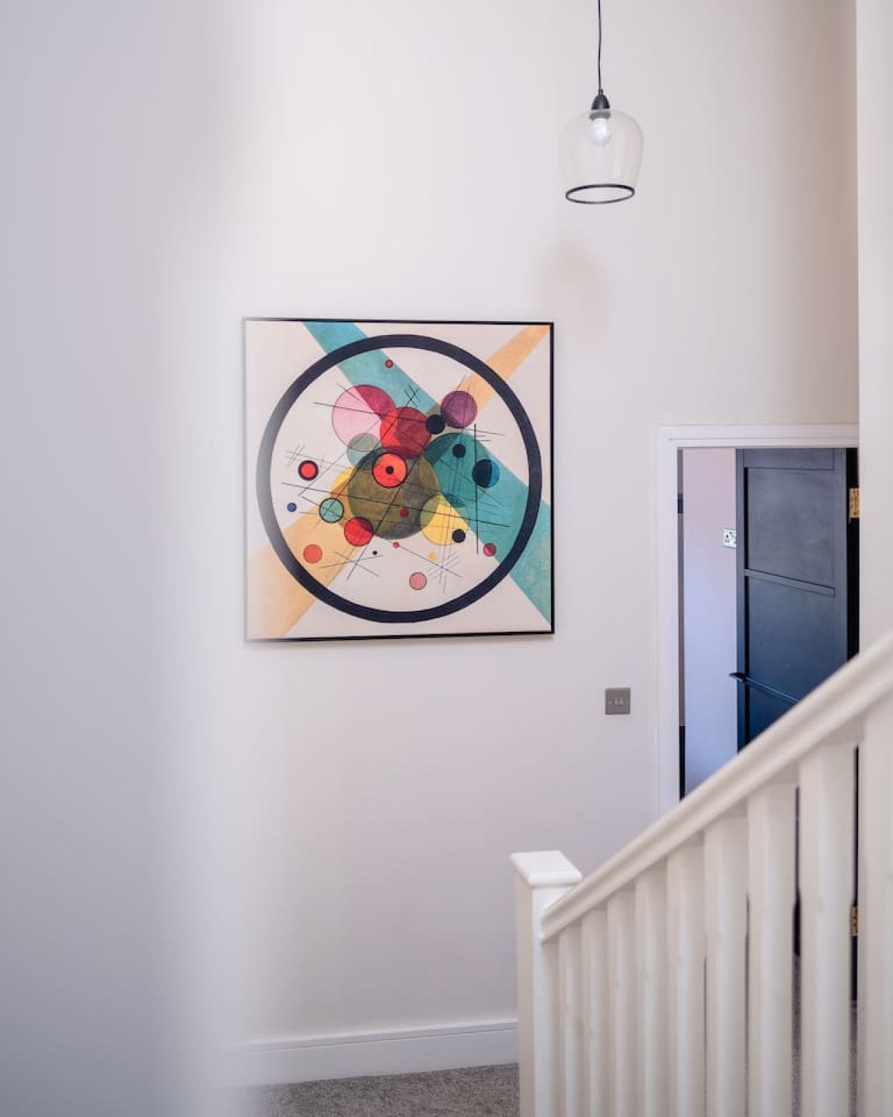 Un passadís amb un quadre abstracte modern a la paret, una barana blanca i una porta al fons.