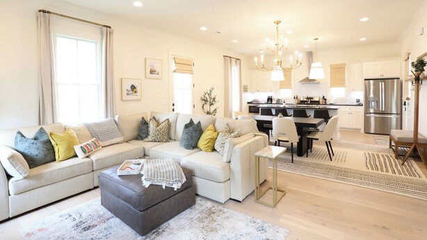 A modern living room with a sectional sofa, ottoman, and a dining area with a table and chairs.
