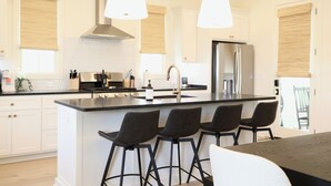 A modern kitchen with a central island, bar stools, stainless steel appliances, and pendant lighting.