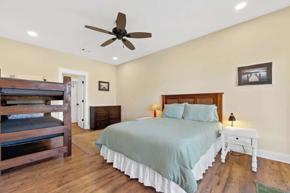 A bedroom with a bed, a wooden bench, a nightstand, a lamp, and a ceiling fan.