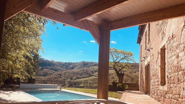 Ein Whirlpool mit Pool, eine Holzpergola, eine Steinmauer und Blick auf eine Berglandschaft.