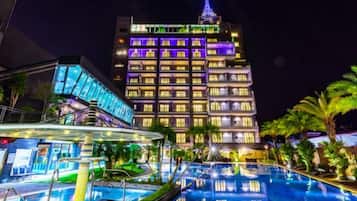 A hotel with a swimming pool, a modern building with illuminated windows, and a tower with a spire.