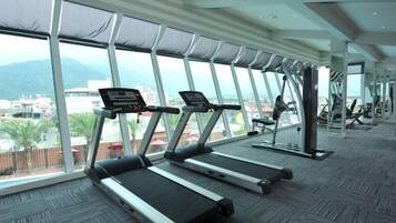 Une salle de sport équipée de tapis de course et d’appareils d’exercice, dotée de grandes fenêtres et offrant une vue sur le paysage urbain.