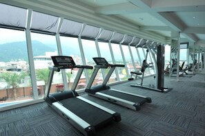 A gym with treadmills and exercise equipment, large windows, and a view of a cityscape. - Cheng Wan Grand Hotel (Nantou)