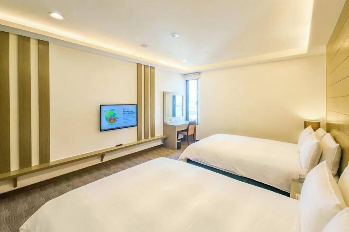 Habitación de hotel con dos camas, un televisor montado en la pared y un escritorio con silla.