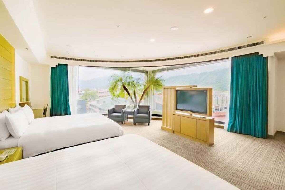 Habitación de hotel con una cama grande, televisión, una mesita, dos sillas y vistas al exterior.