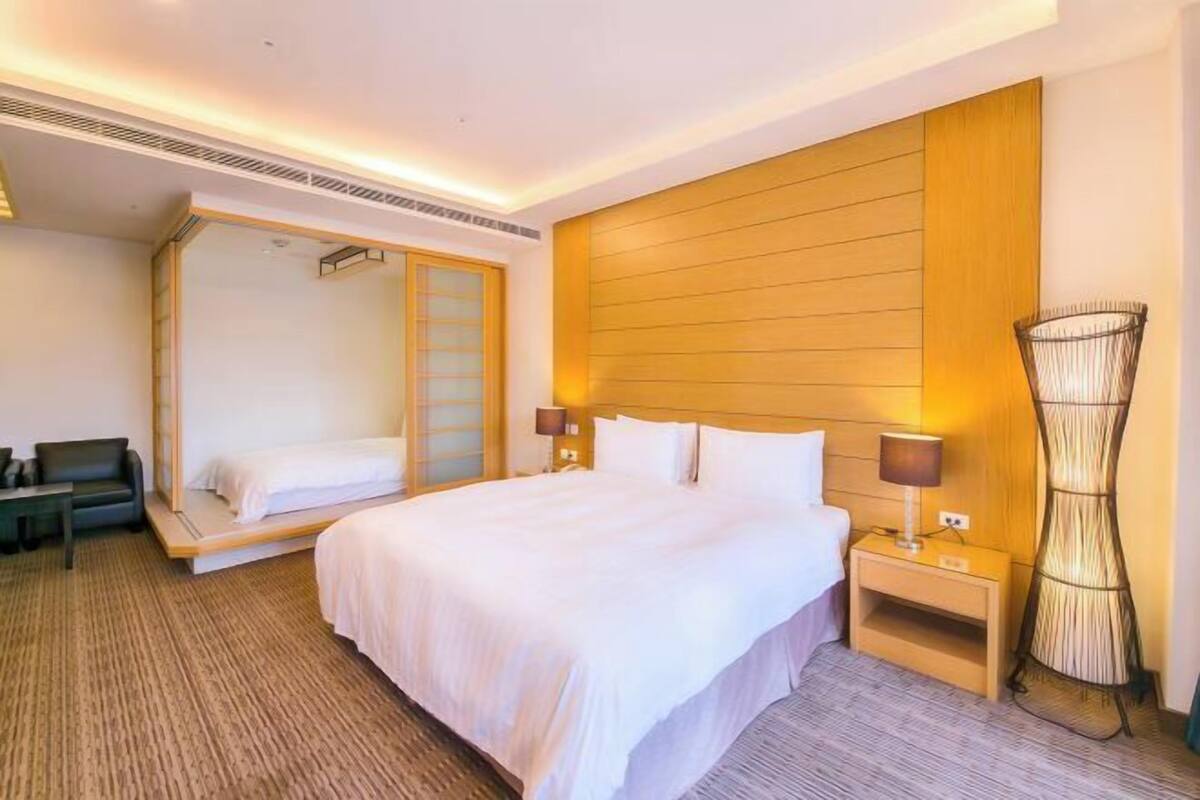 Una habitación de hotel con una cama grande, mesitas de noche, un sofá, un espejo y una lámpara de pie original.