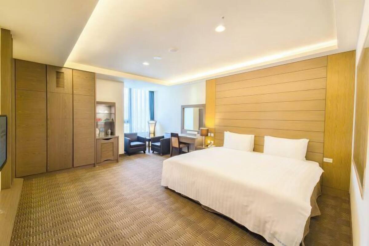 Una habitación de hotel con una cama grande, un escritorio con silla, un armario y un televisor.