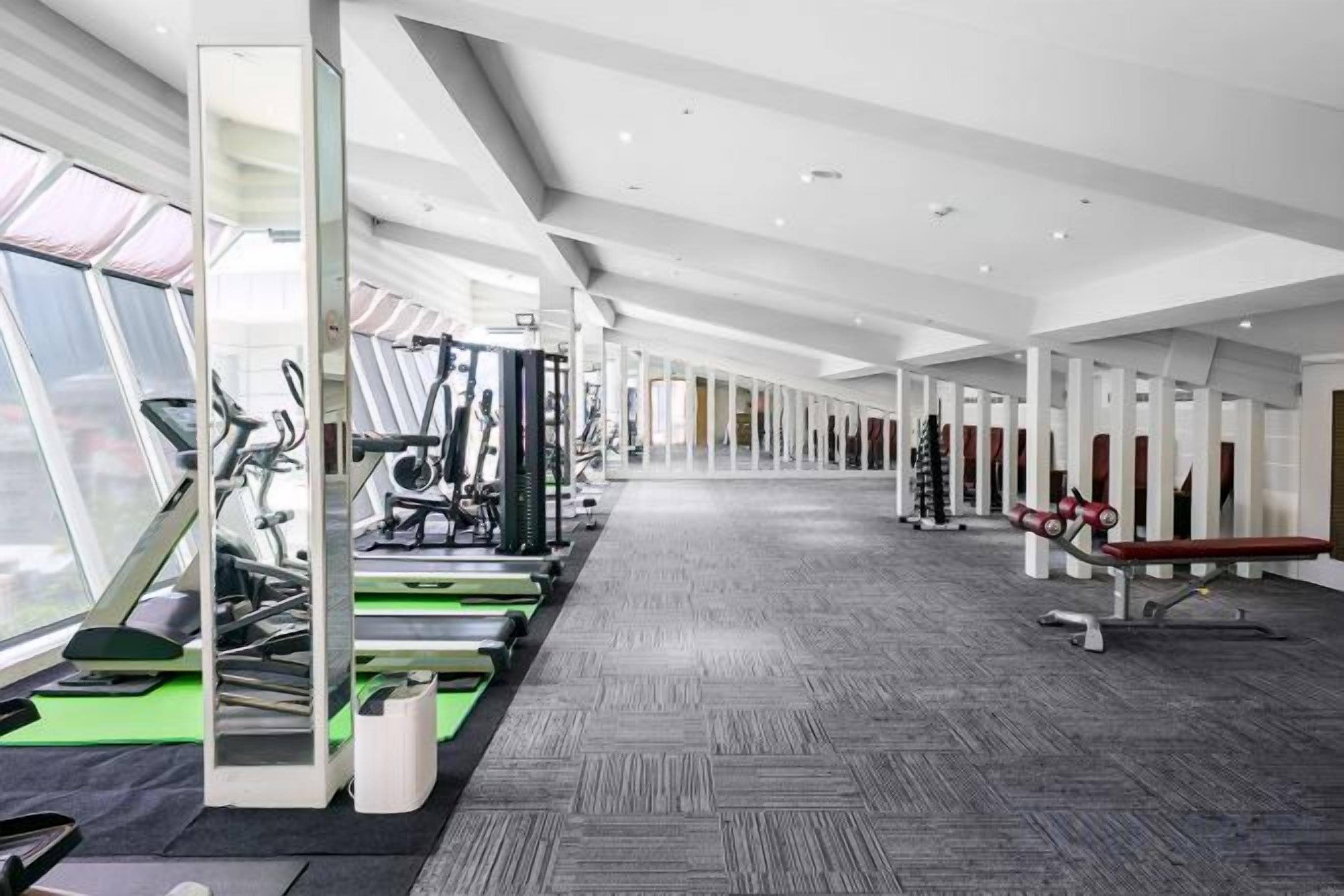 A gym with cardio machines, weightlifting equipment, and a mirrored wall.