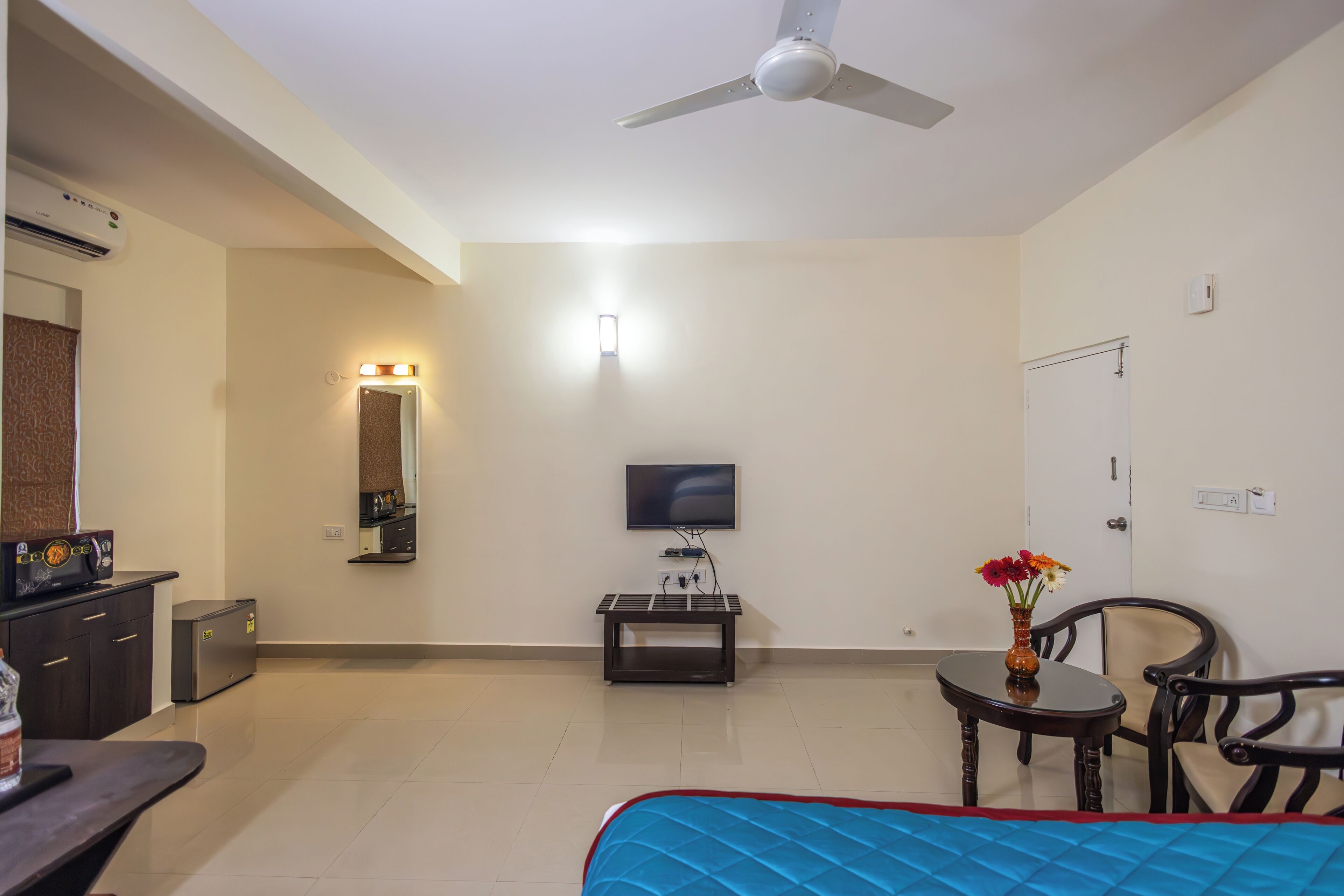 Habitación de hotel con cama, televisión, escritorio, silla, mesa y ventilador de techo.