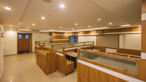 A modern hotel lobby with wooden reception desks, a seating area, and a large window with blinds. - Suraksha Stay Brookfield  (Bengaluru)