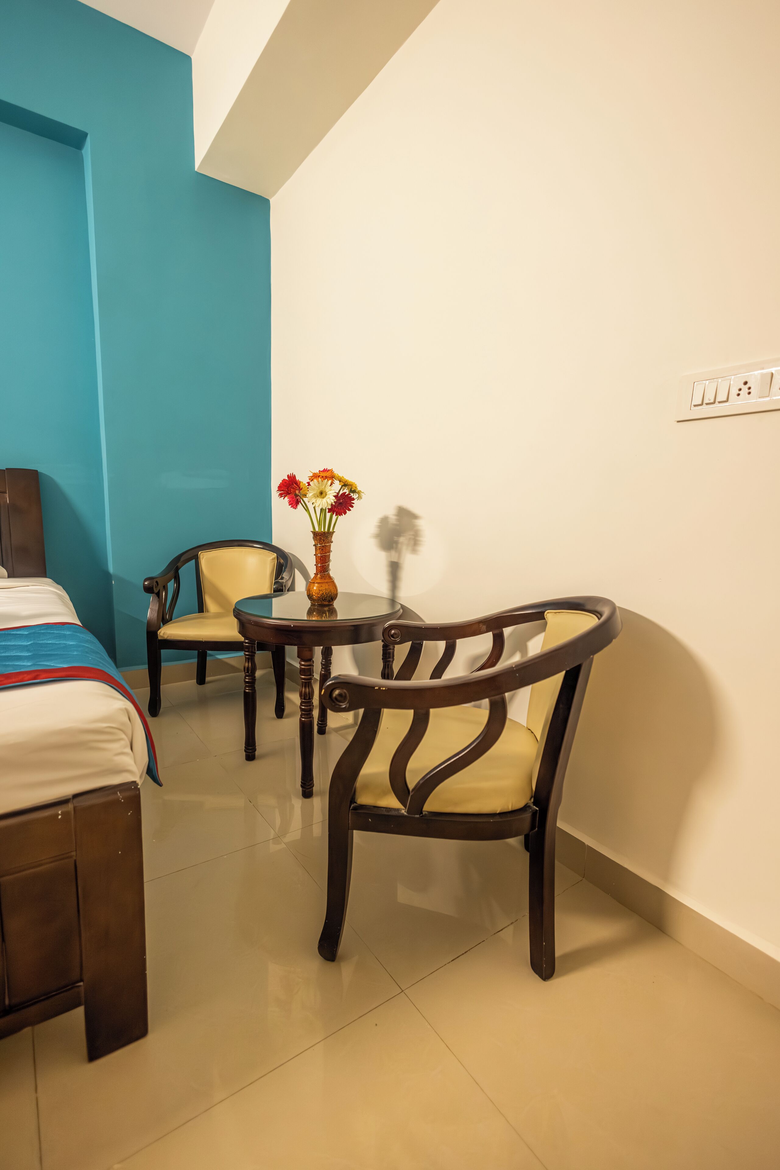 Une chambre d’hôtel avec un lit, deux chaises, une petite table avec un vase et un mur d’accent bleu.