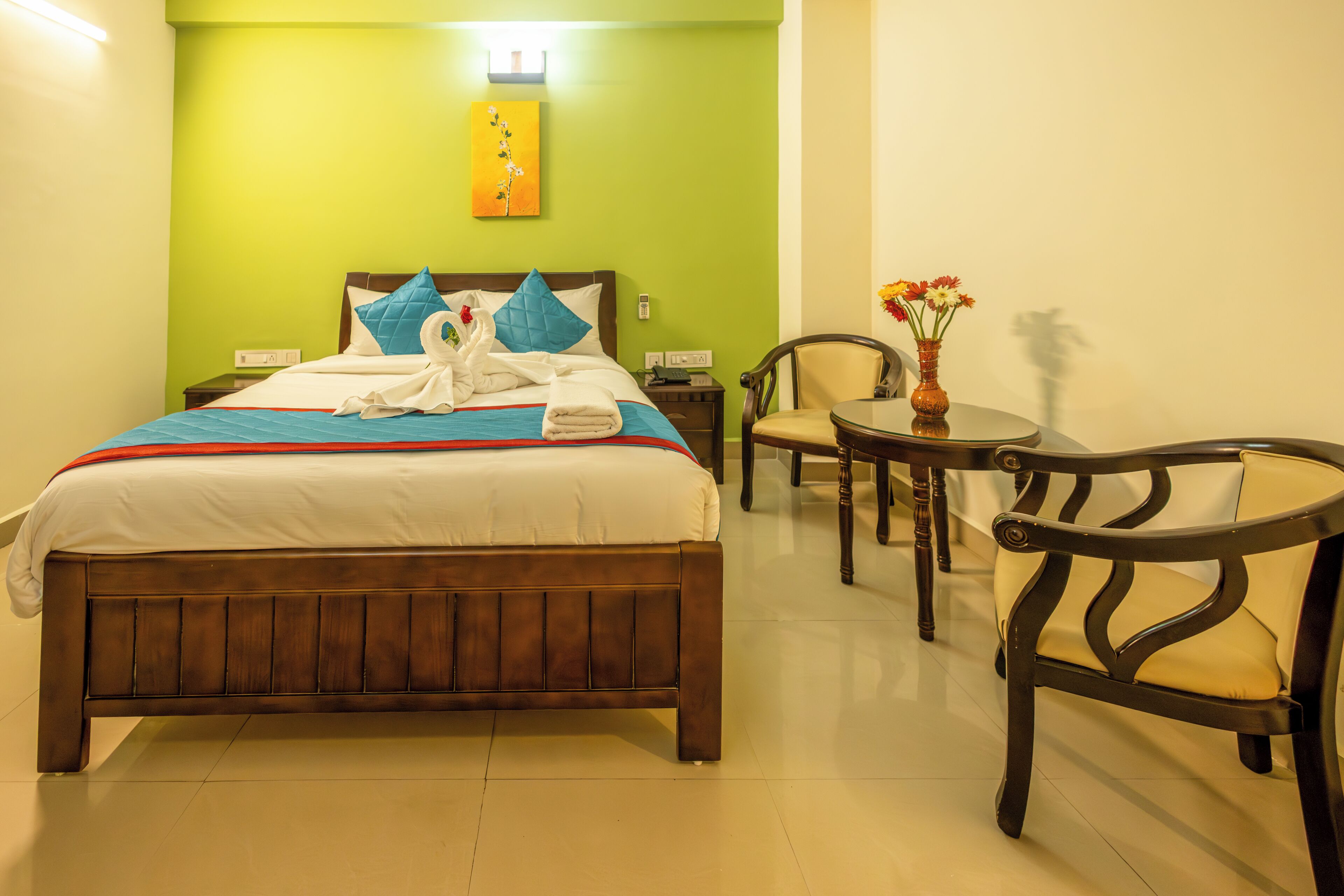 Une chambre d’hôtel avec un lit, une chaise, une petite table et un vase de fleurs.