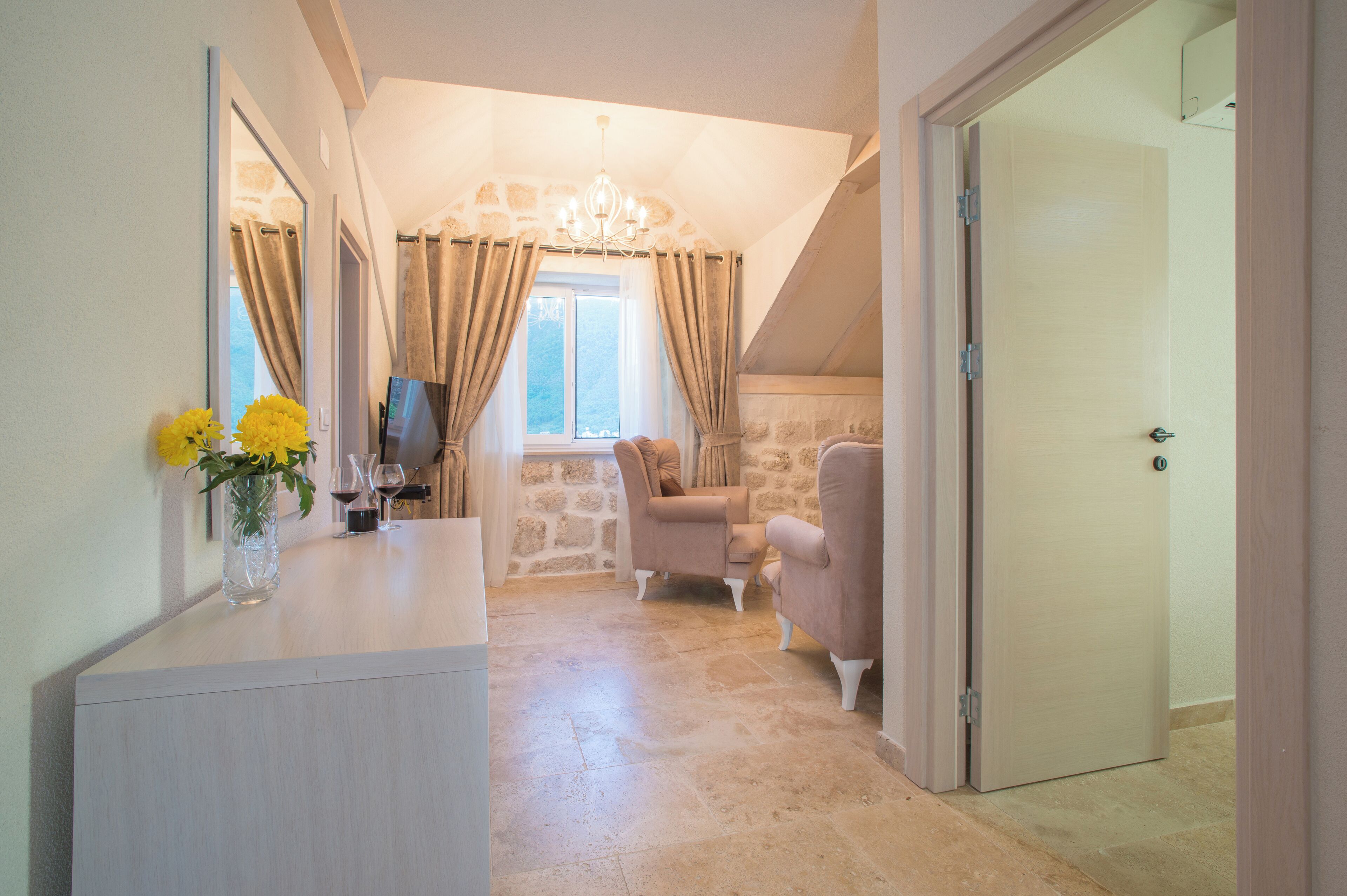 A room with a stone wall, a chandelier, a TV, a sofa, and a door.