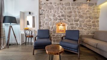 Una sala de estar acogedora con una pared de piedra, dos sillones azules, una mesa de centro de madera, un escritorio blanco y un sofá beige.